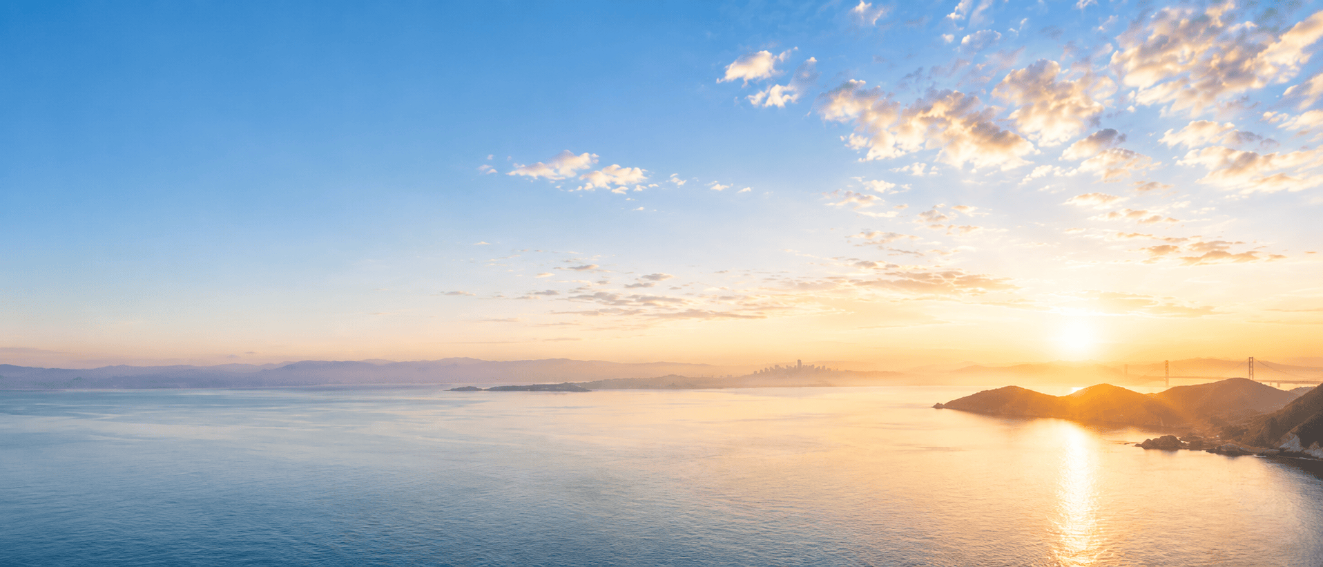 Golden Gate Bridge and San Francisco Bay skyline at sunrise with a bright blue sky